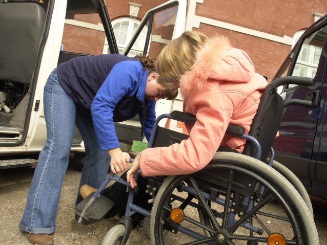 asystentka pomaga kobiecie na wózku przetransporować się do samochodu