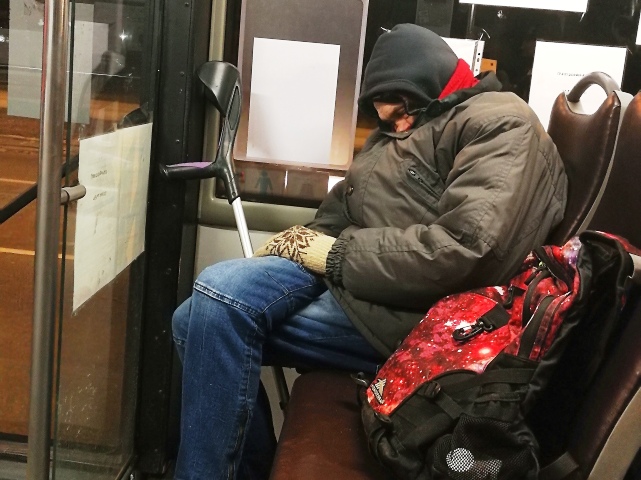 śpiący mężczyzna w autobusie, obok stoją jego kule, a na drugim siedzeniu leży plecak